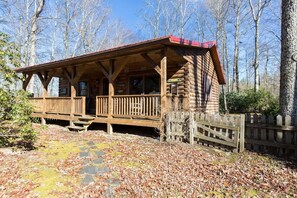 Ein rustikales Blockhaus mit Veranda, umgeben von einem Holzzaun und einem mit Laub bedeckten Boden.