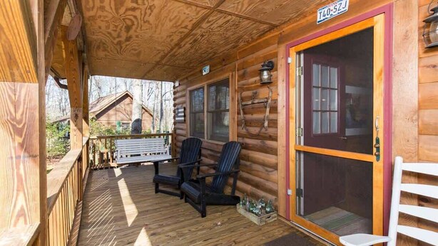 Eine Holzhütte mit Veranda, zwei Stühlen, einer Bank und einer Tür mit einer Nummer.