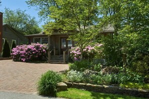 A residential house with a brick driveway, surrounded by lush greenery and flowering plants. - Bark Bungalow (Blowing Rock)