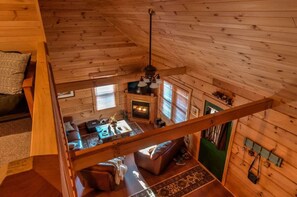 Interior de cabana com quarto em mezzanine, lareira, área de refeições e um espaço de estar acolhedor.