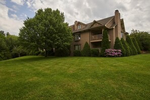 A two-story house with a balcony, surrounded by a well-maintained lawn and various trees.