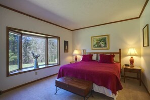 A bedroom with a large window, a bed with red bedding, two bedside lamps, and a wooden bench.