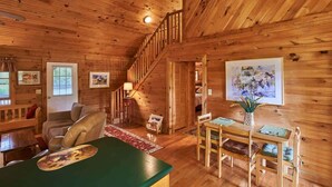 Ein gemütliches Blockhäuschen mit Holzvertäfelung, einer Treppe, einem Essbereich und einem Wohnzimmer mit Kamin.
