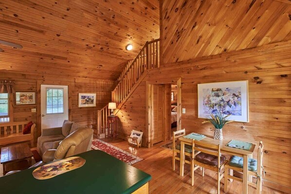 L’intérieur chaleureux d’un chalet, avec un décor en bois, un escalier, un coin repas et un salon doté d’une cheminée.