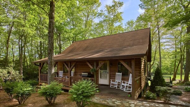 Ein rustikales Holzhaus mit Veranda, umgeben von Bäumen und einem Steinweg.
