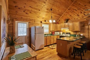 L’intérieur d’une cabane en bois comprend une cuisine équipée de meubles en bois, d’un réfrigérateur, d’un four à micro-ondes et d’un coin repas avec une table et des chaises.