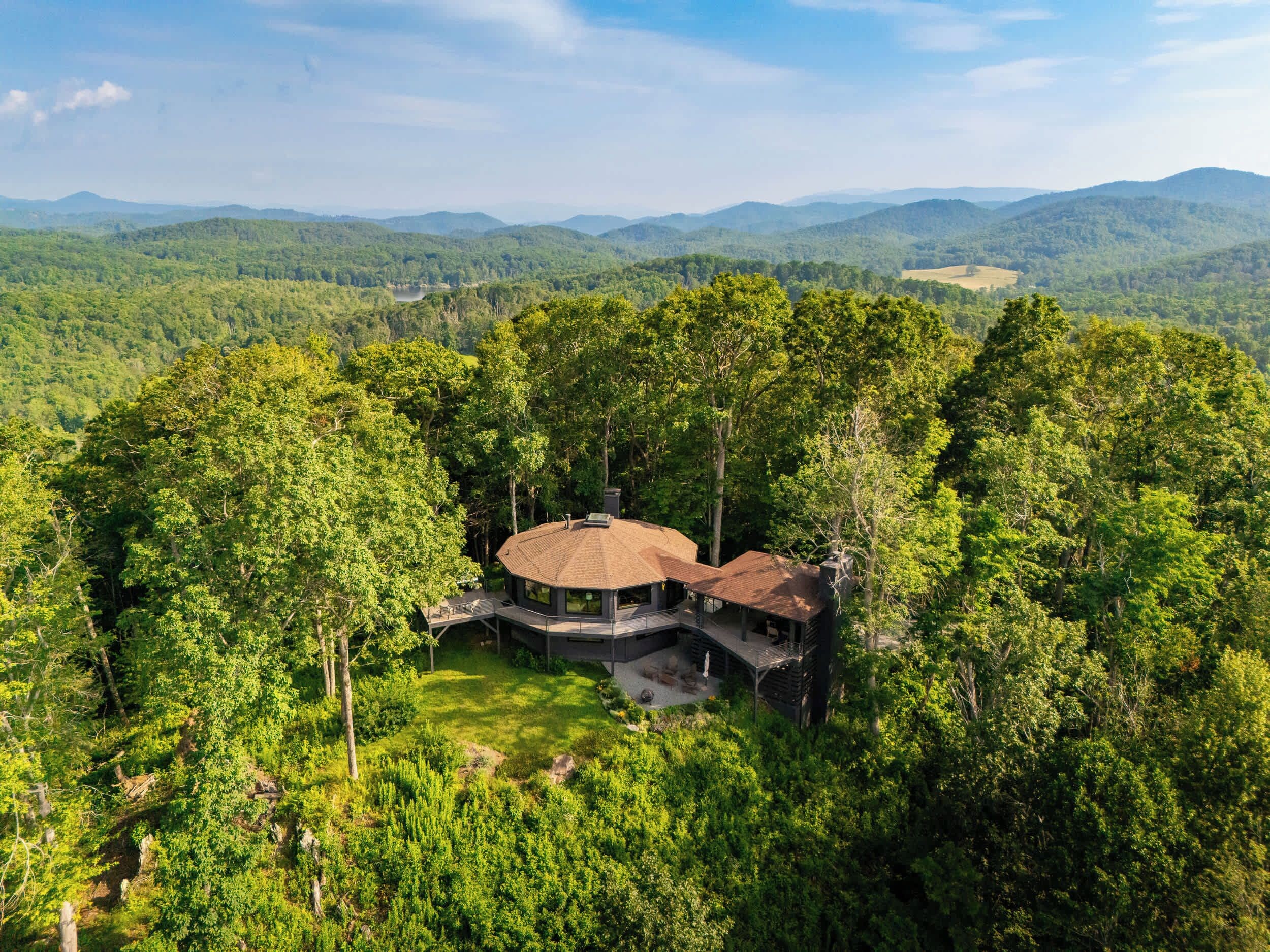 A secluded cabin surrounded by dense forest, with a circular roof and a deck area.