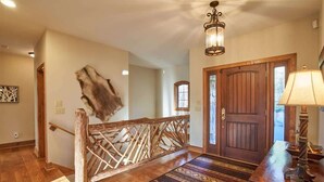 Eine Holztreppe mit dekorativer Geländer, einem gemusterten Teppich, einer Holztür und einem Tisch mit Lampe.