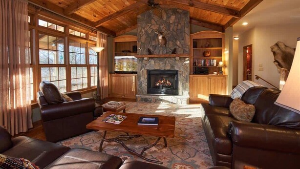 Ein gemütliches Wohnzimmer mit Ledersofas, einem Kamin aus Stein und Holzbalken an der Decke.
