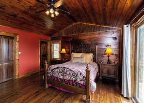 A wooden-paneled bedroom with a bed, two bedside lamps, and a ceiling fan.