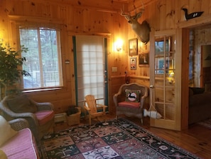 Interior acolhedor de uma cabana, com paredes de madeira, um chifre de veado montado na parede, um tapete estampado e uma poltrona com almofada.