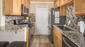 A compact kitchen with wooden cabinets, a microwave, a refrigerator, and a tiled backsplash. - Bearway to Heaven - 2BR/2BA Condo, Downtown BR (Blowing Rock)