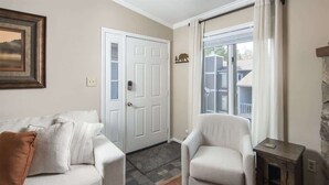 A living room with a white sofa, a white armchair, a door, and a window with curtains. - Bearway to Heaven - 2BR/2BA Condo, Downtown BR (Blowing Rock)