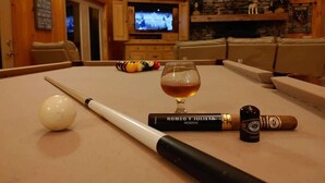 A pool table with a cue ball, a cue stick, a glass of whiskey, and a cigar.