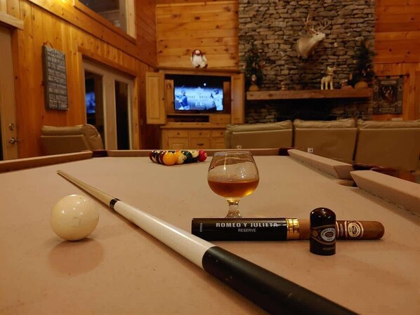 Une table de billard avec une boule blanche, une queue de billard, un verre de whisky et un cigare.