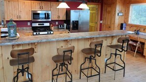 A kitchen with wooden cabinets, stainless steel appliances, a granite countertop, and bar stools.