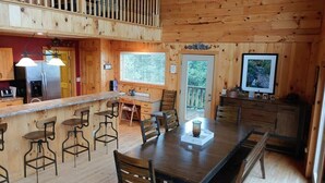 A wooden cabin interior with a dining area, kitchen, and a balcony.