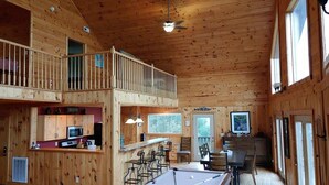 A wooden cabin with a pool table, bar area, and a loft with a balcony.
