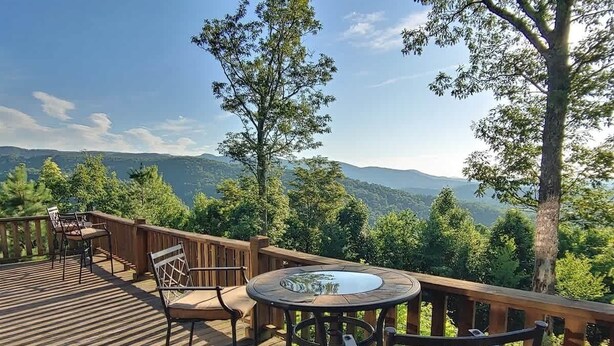 A wooden deck with a round table and chairs, overlooking a mountainous landscape.