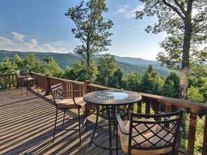 Une terrasse en bois avec une table ronde et des chaises, offrant une vue sur un paysage montagneux.