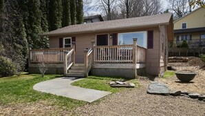 Einbungalow mit Veranda, Betonauffahrt und Kiesfläche mit einem großen Stein.