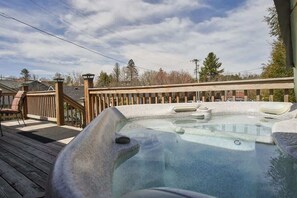 Een hottub op een houten terras met een houten leuning en een uitzicht op bomen en huizen op de achtergrond.