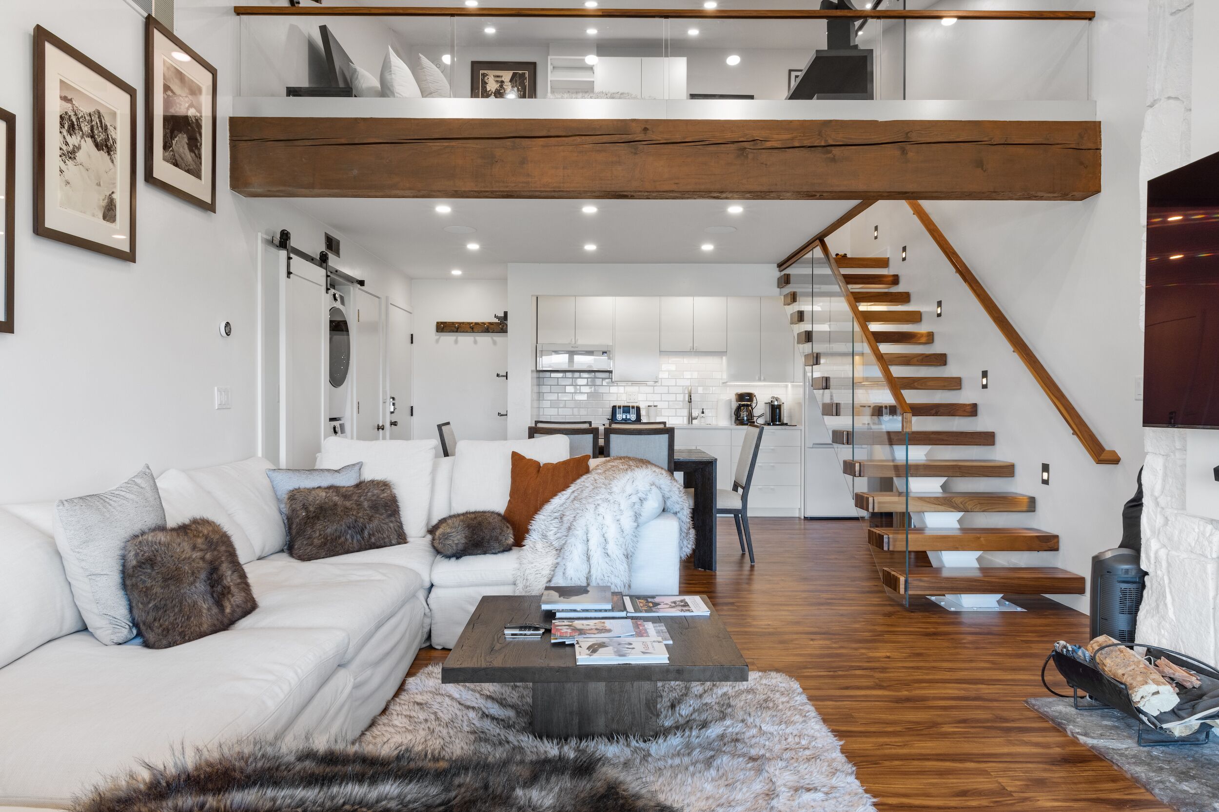 Una sala de estar moderna con un sofá blanco, una mesa de centro y una escalera que lleva a un nivel superior.