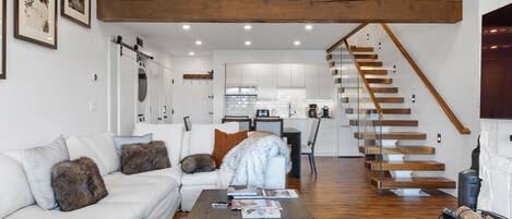 Una sala de estar moderna con un sofá blanco, una mesa de centro y una escalera que lleva a un nivel superior.