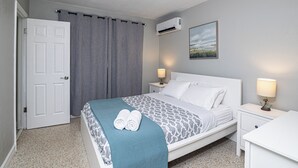 Une chambre à coucher bien rangée, avec un lit, deux tables de chevet avec des lampes, une porte et un climatiseur fixé au mur.