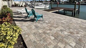 Une terrasse au bord de l’eau, avec des chaises, un quai et des bateaux.