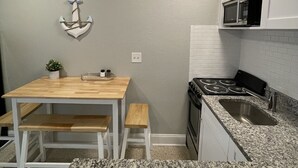 Une cuisine compacte avec une table en bois, des placards blancs, un plan de travail en granit et un four à micro-ondes placé au-dessus de l’évier.