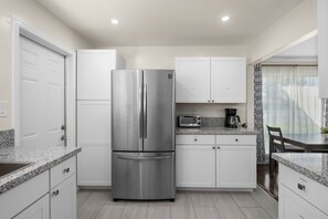 A modern kitchen with white cabinets, a stainless steel refrigerator, a built-in oven, and a granite countertop.