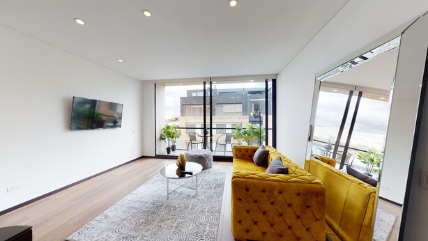 Ein modernes Wohnzimmer mit einem gelben Sofa, einem Flachbildfernseher und großen Fenstern mit Blick auf die Stadt.