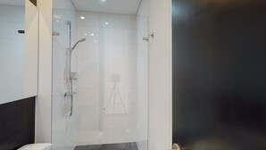 Ein modernes Badezimmer mit Duschkabine aus Glas, Toilette und einer dunkel gefärbten Tür.