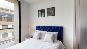Ein modernes Hotelzimmer mit einem großen Bett, weißer Bettwäsche, einem blauen Kopfteil und zwei gerahmten Bildern an der Wand.