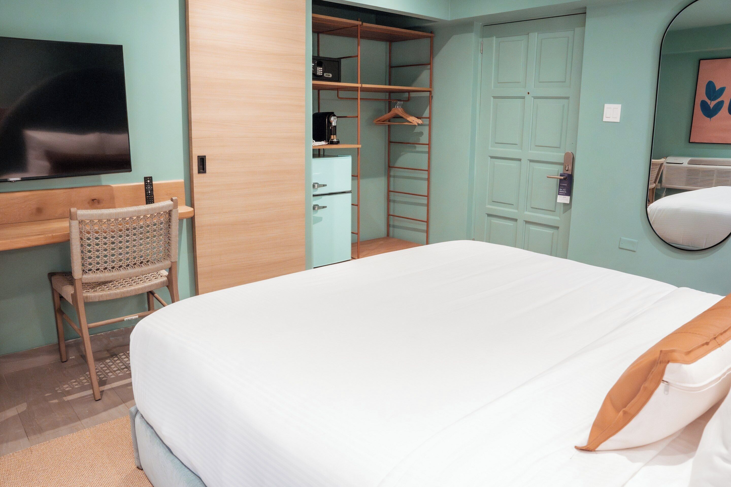 A bedroom with a bed, a desk, a chair, a wardrobe, and a television.