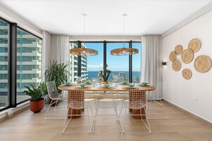 Un comedor moderno con un ventanal grande, dos lámparas colgantes, una planta en maceta y una mesa preparada para cuatro.