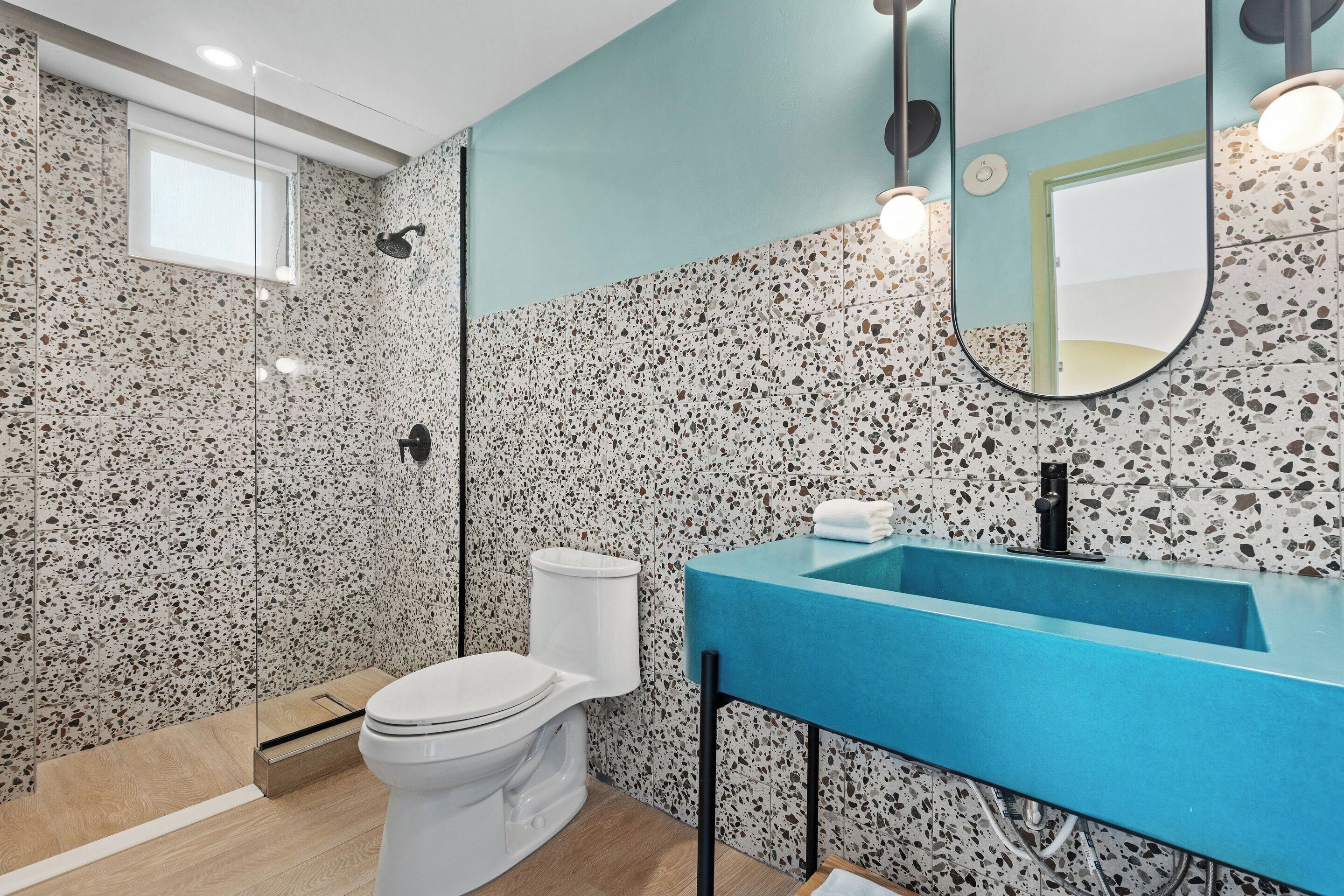 A modern bathroom with a white toilet, a blue sink, and terrazzo walls.