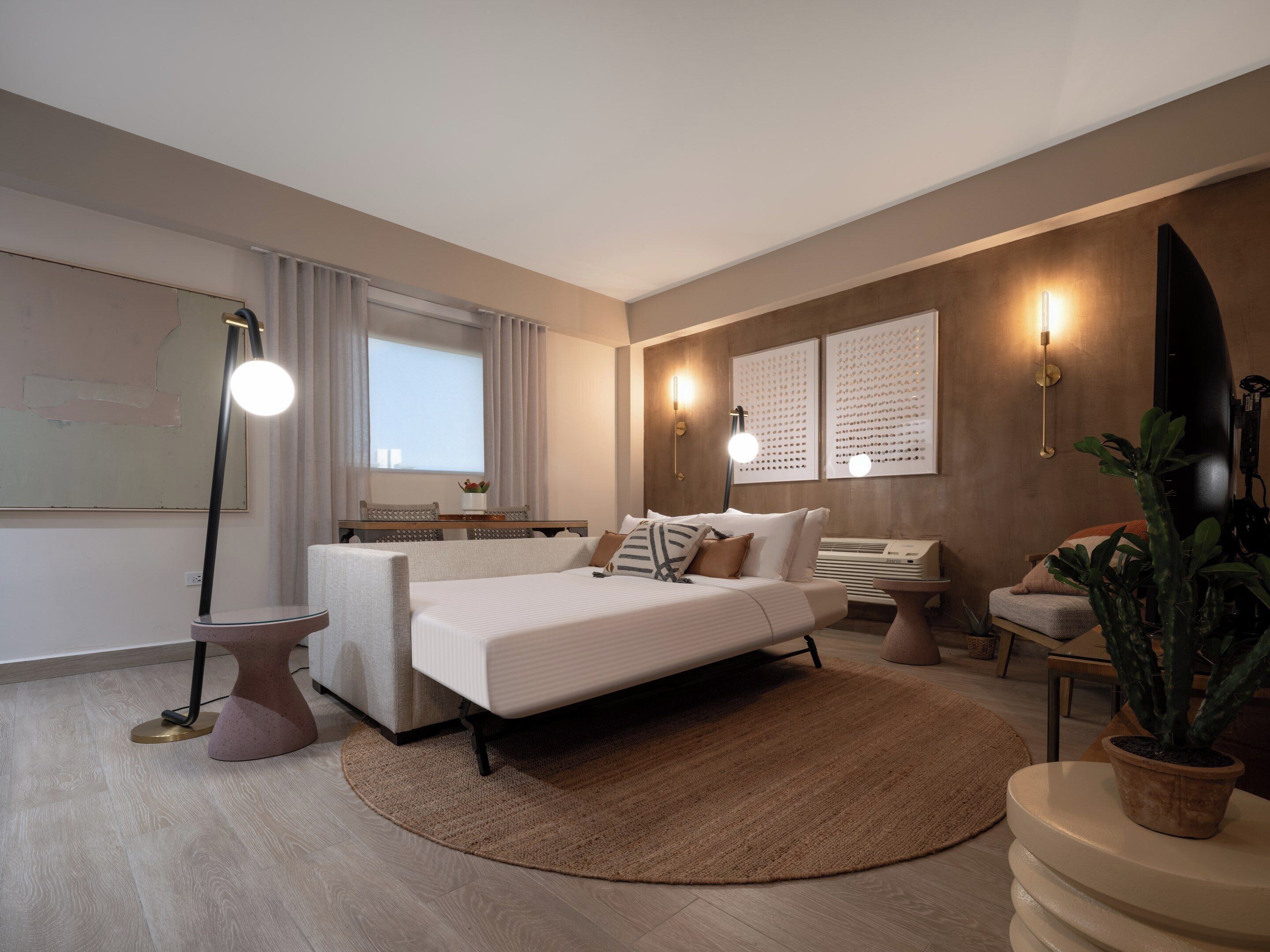 Une chambre à coucher moderne avec un lit, des lampes de chevet, un bureau et une plante en pot.