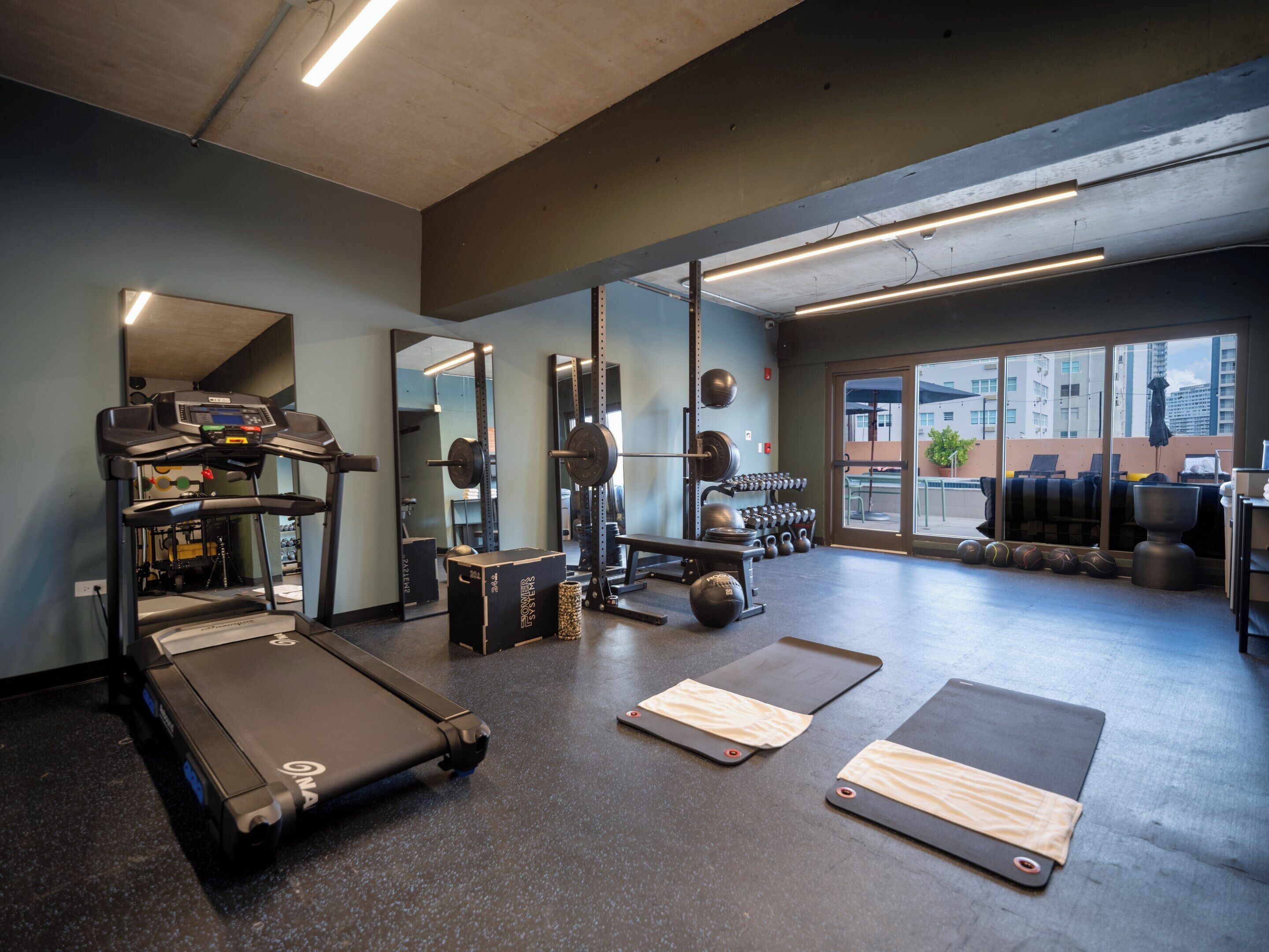 Un gimnasio con cintas de correr, equipo de levantamiento de pesas y colchonetas de yoga.
