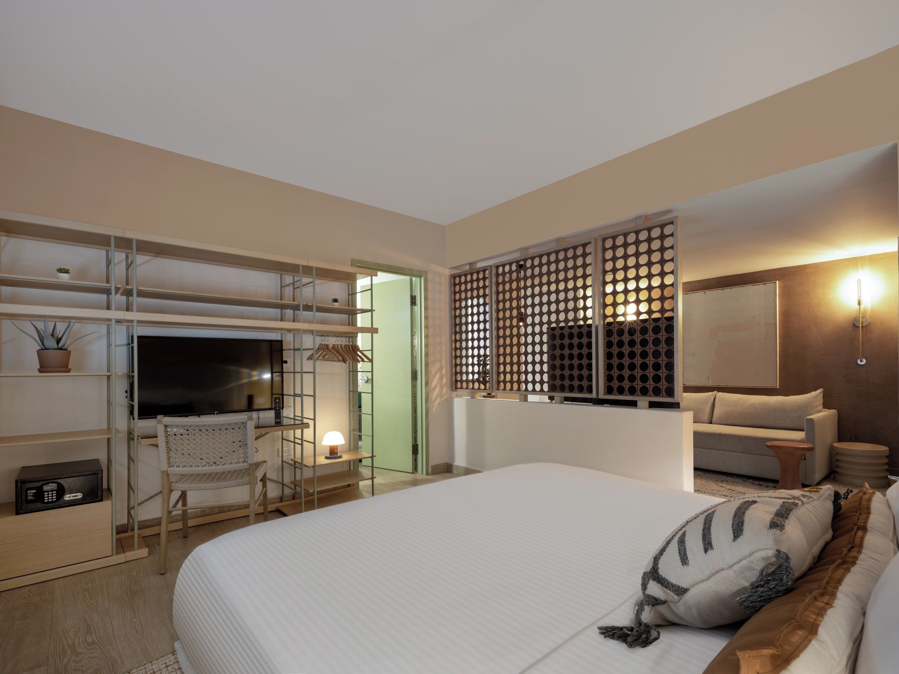 A hotel room with a bed, a TV, a desk with a chair, a sofa, and a decorative screen.