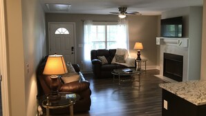 Un salon avec un canapé en cuir, une table basse en verre, une cheminée et un ventilateur de plafond.