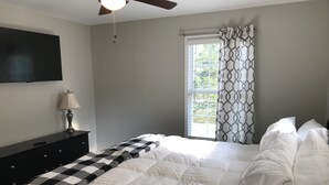 Une chambre à coucher comprenant un lit, une table de chevet, une lampe, un ventilateur de plafond et une fenêtre avec des rideaux.