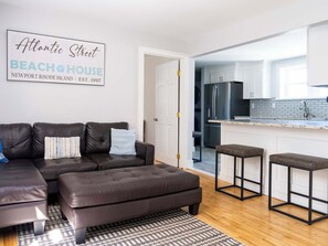 A modern living room with a leather sofa, a patterned rug, and a kitchen with white cabinets and stainless steel appliances.