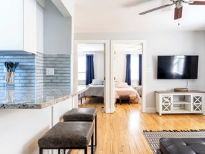 A modern living space with a kitchen, a dining area, a bedroom, and a TV mounted on the wall.