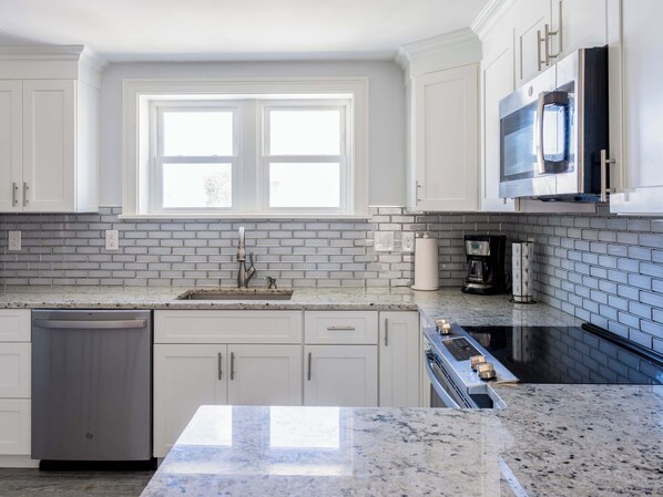 A modern kitchen with white cabinets, a granite countertop, a double sink, a dishwasher, a stove, and a microwave.