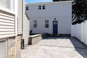 A two-story building with a blue door, a stone wall, and a paved driveway.
