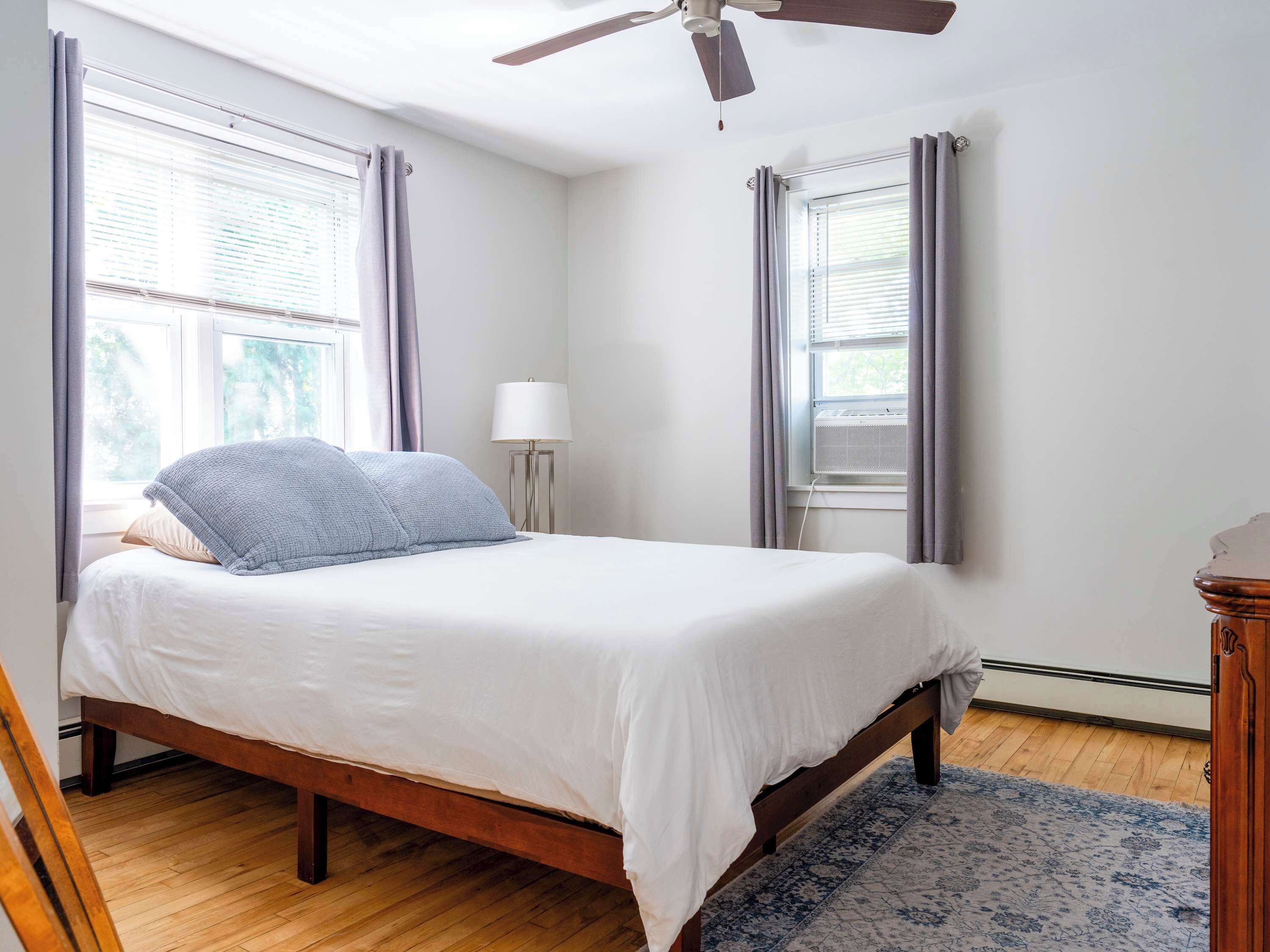 Un dormitorio con cama, ventilador de techo, ventana con cortinas, lámpara de pie y radiador.