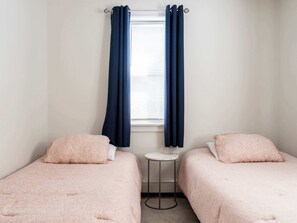 A room with two beds, a small table, and a window with curtains.