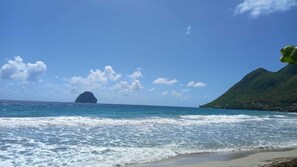 A beach with waves, a distant island, and a green hill.